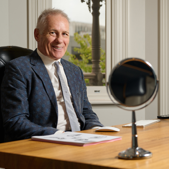 Smiling man in a suit sitting at a desk in an office with a mirror in front | Dr. Rodger Davies
