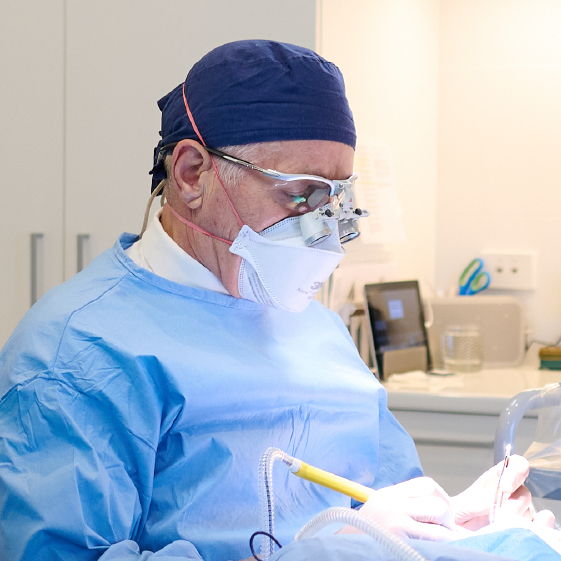 Surgeon wearing scrubs, mask, and magnification glasses while performing surgery | Dr. Rodger Davies