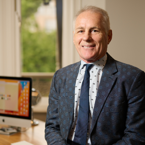 Man in a patterned suit sitting at a desk with a computer in the background | Dr. Rodger Davies